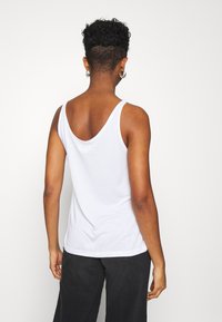 White cotton tank top with wide shoulder straps and a scoop back. The fabric is smooth, lightweight, and fitted at the waist.