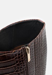 Sac à main en cuir marron embossé crocodile avec un intérieur lisse et une fermeture éclair dorée, présentant une forme structurée et rectangulaire.