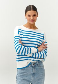 Gestreepte gebreide trui in wit en blauw. Ronde hals, lange mouwen, geribde boorden en zoom. Gecombineerd met hoge taille spijkerbroek.