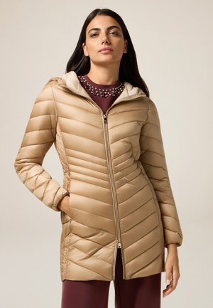 Beige pufferjack met chevronstiksel, ritssluiting en een capuchon. Lichtgewicht, glanzende stof met geribbelde textuur en zijzakken.