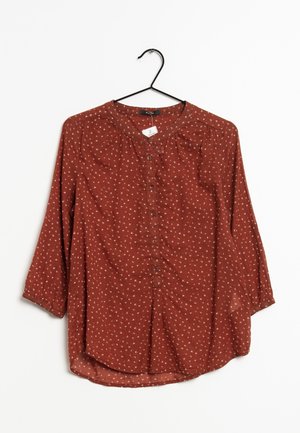 Bluse in Rostfarbe mit kleinem weißem Blumenmuster, vorne geknöpft, mit dreiviertellangen Ärmeln, an einem schwarzen Kleiderbügel vor weißem Hintergrund hängend.