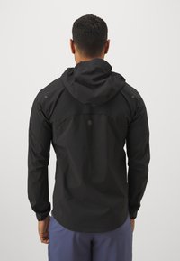 Chaqueta ligera negra con capucha, de textura suave y diseño ajustado. Presenta un hardware mínimo y un dobladillo sutilmente curvado.