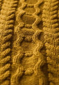 Närbild av gult stickat tyg med texturerade flätmönster som löper vertikalt.