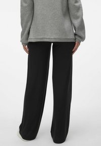 Sweatshirt gris surdimensionné avec manches longues, associé à un pantalon noir côtelé à taille haute. La tenue a une coupe décontractée et confortable.