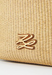Woven beżowa torba z złotym i brązowym akcentem logo. Tekstura jest gładka, a kształt ma wyraźną formę z misternym wzorem tkania.