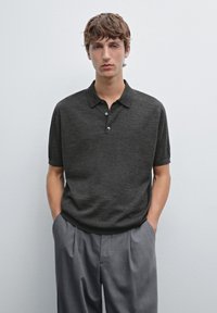 Polo a maniche corte grigio scuro con tre bottoni, texture a maglia e colletto. Abbinato a pantaloni grigi chiari. Design semplice e minimalista.