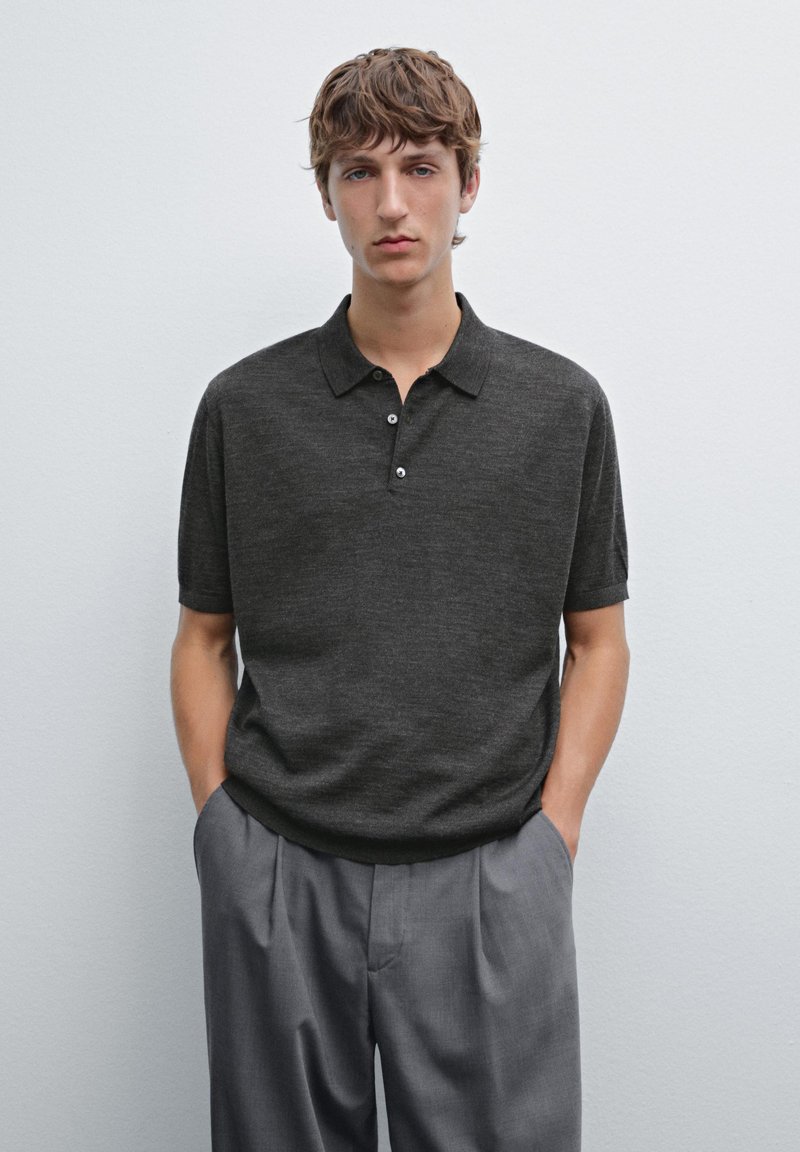 Polo a maniche corte grigio scuro con tre bottoni, texture a maglia e colletto. Abbinato a pantaloni grigi chiari. Design semplice e minimalista.