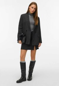 Šedý dvouřadý blejzr přes přiléhavý šedý rolák, doplněný o tmavou tužkovou sukni s bočním rozparkem a vysokými černými kozačkami.