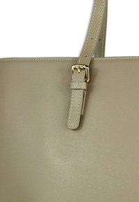 Beige boodschappentas van getextureerd leer, voorzien van een veilige gesp in goudkleurige toon en stikselaccenten op de riem.