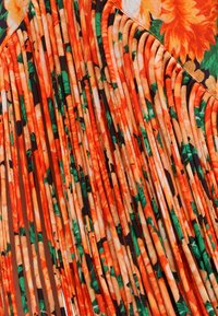 Φωτεινό πορτοκαλί και πράσινο υφασμάτινο σχέδιο με στενά πλισέ υφή που δημιουργεί κατακόρυφες γραμμές πάνω στο υλικό.