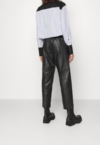 Schwarze Lederhosen mit lässiger Passform, kombiniert mit einem gestreiften Langarmshirt mit schwarzem Schulterbereich und knöpfbaren Manschetten.