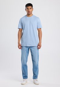 Light blue short-sleeve t-shirt, crew neck, cotton material, relaxed fit. Paired with light wash jeans and white sneakers.