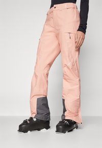 Light pink snow pants with a tapered fit, featuring gray accents at the cuffs, zippered side pockets, and durable waterproof material.