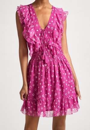 Ærmeløs pink kjole med flæser, bindebånd ved halsen, smock omkring taljen og et diamantmønster, båret af en stående person.