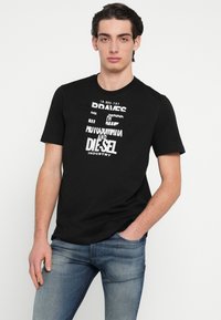 Čierne bavlnené tričko s bielym potlačeným textom na prednej strane. Krátke rukávy, okrúhly výstrih a voľný strih. Nosené s modrými rifľami.