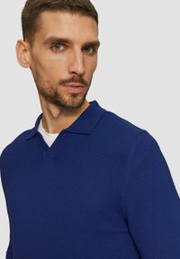 Niebieska polo z teksturowanej tkaniny, z dekoltem w serek i krótkimi rękawami, w jednolitym kolorze z subtelnym wzorem.