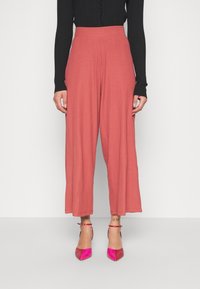 Wijdvallende, lichtroze broek van een gestructureerde stof, met een hoge elastische tailleband. Gecombineerd met glanzende, roze puntige hakken.