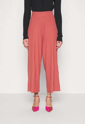 Breda ben, ljusrosa byxor i texturerat tyg med hög elastisk midja. Matchat med glansiga, rosa spetsiga klackskor.