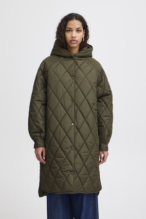 Manteau long matelassé vert olive avec capuche. Présente des coutures en losange, des fermetures à boutons-pression et des manches larges. Le tissu semble texturé et isolant.