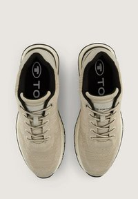 Zapatillas de punto beige con parte superior texturizada, forro interior negro y suela blanca con una franja negra. Logo visible en la lengüeta.