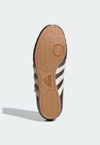 Zwarte sportschoen zool met een getextureerde rubberen grip, drie witte strepen en een geperst logo. Rondneus en een glad materiaal aan de buitenkant.