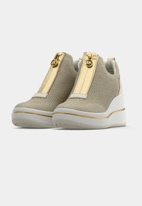 Beiget kiilatennarit, joissa on verkkokankainen päällinen, kultainen vetoketjusomiste ja valkoinen pohja kultaisella raidalla. Kevyt ja teksturoitu muotoilu.