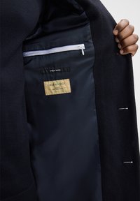 Wollen jas interior met een donkere voering, met een ritszak en labels met de teksten "FINest WOOL" en "GREENWOOL."