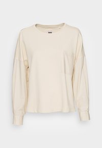 Camicetta a maniche lunghe, di colore crema, realizzata in tessuto morbido, con scollatura arrotondata e taschino sul petto; presenta maniche ampie e plissettate.
