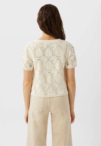 Cream-colored knitted sweater with short sleeves, featuring a textured lace pattern and subtle floral embroidery on the shoulders.