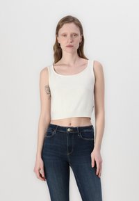 White cropped tank top with a round neckline and ribbed hem, paired with dark blue high-waisted jeans featuring visible stitching and button closure.