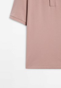 Polo en tissu rose poudré, manches courtes, col avec patte de boutonnage à trois boutons, finition texturée et ourlet droit.