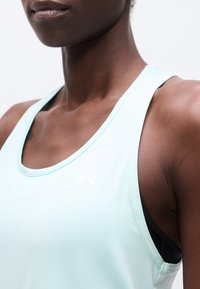 Gros plan sur une personne portant un débardeur Under Armour bleu clair par-dessus un soutien-gorge de sport noir, montrant l'épaule et le haut de la poitrine.