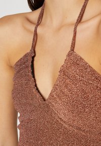 Zbliżenie na osobę w błyszczącej miedzianej bluzce na ramiączkach z falbanastymi brzegami i głębokim dekoltem w kształcie litery V.