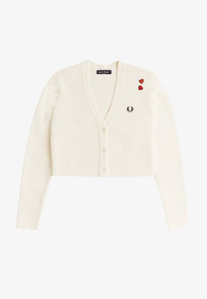 Valkoinen lyhyt neuletakki V-pääntiellä, kolmella napilla, pienellä mustalla laakeriseppelelogolla rinnassa ja kahdella punaisella sydänlaastarilla vasemmalla olkapäällä.