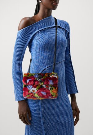 Borsa a tracolla in pelliccia colorata con una texture morbida. Presenta una chiusura nera e una tracolla a catena, abbinata a un vestito blu a coste.