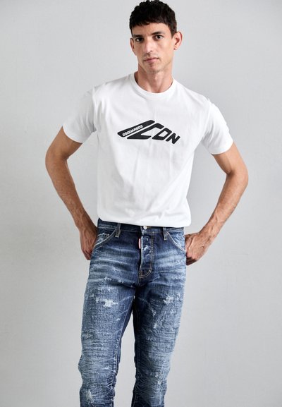 White crew-neck t-shirt with black "DSQUARED2" logo, paired with distressed blue denim jeans featuring faded patterns and stitching accents.