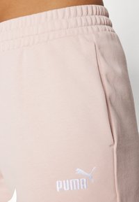 Light pink joggers with an elastic waistband, featuring front pockets and subtle branding. Smooth texture with a soft cotton blend.