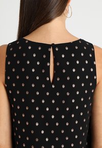 Robe en tissu noir avec un motif à pois en rose métallisé, dotée d'une petite ouverture en forme de clé à l'arrière et d'une fermeture par bouton.