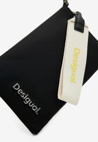 Clutch in nylon nero con logo argento, dotato di una tracolla crema con testo giallo. Forma rettangolare con superficie liscia e chiusura a zip.
