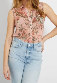 Camiseta sin mangas con estampado floral en rosa suave con motivos botánicos en verde y blanco; combinada con vaqueros de tiro alto en azul claro.