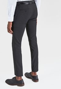 Pantalones negros de corte a medida, hechos de un tejido suave, con un ajuste slim, bolsillo trasero abotonado y combinados con zapatos brogue negros.