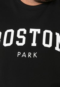 Svart t-shirt med fet vit text som står "BOSTON PARK", med rund hals och korta ärmar, tillverkad av mjukt bomullsmaterial.