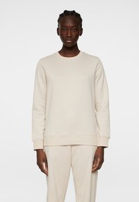 Crème-kleurige sweatshirt met een klassieke ronde hals, ribgebreide mouwen en zoom, gemaakt van zachte stof. Beschikt over een subtiele logo op de borst.