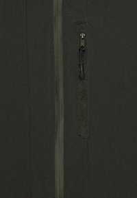 Tummanvihreä fleece-takki, jossa on sileä pinta, täyspitkä vetoketju ja vetoketjullinen tasku edessä, jossa on nyöri.