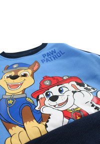 Sweat-shirt bleu avec des chiens de dessin animé, l'un en uniforme de policier et l'autre habillé en pompier, avec le texte "PAW PATROL" imprimé au-dessus.