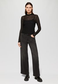 Zwarte kanten top met lange mouwen, een textuurpatroon en een hoge hals, gecombineerd met donkergrijze hoge taille wijde jeans en zwarte platformlaarzen.