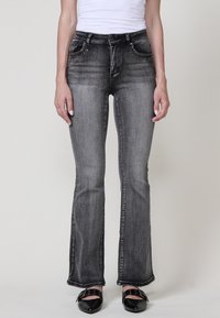 Jeans de campana gris oscuro con un sutil efecto desgastado, adornados con pequeños embellishments en los bolsillos frontales. Hechos de material de mezclilla.