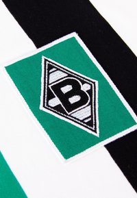Logo bordado que presenta una forma de diamante con una "B" negra sobre un fondo verde, contorneada en blanco. El diseño incluye rayas en blanco y negro.