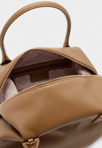 Borsa a mano in pelle marrone con chiusura zip, caratterizzata da una texture liscia e un interno foderato con un tessuto a motivi. Dettagli del logo all'interno.