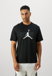 Sort bomulds t-shirt med et stort hvidt Jumpman-logo på brystet, rund hals og korte ærmer. Stoffet har en glat tekstur.